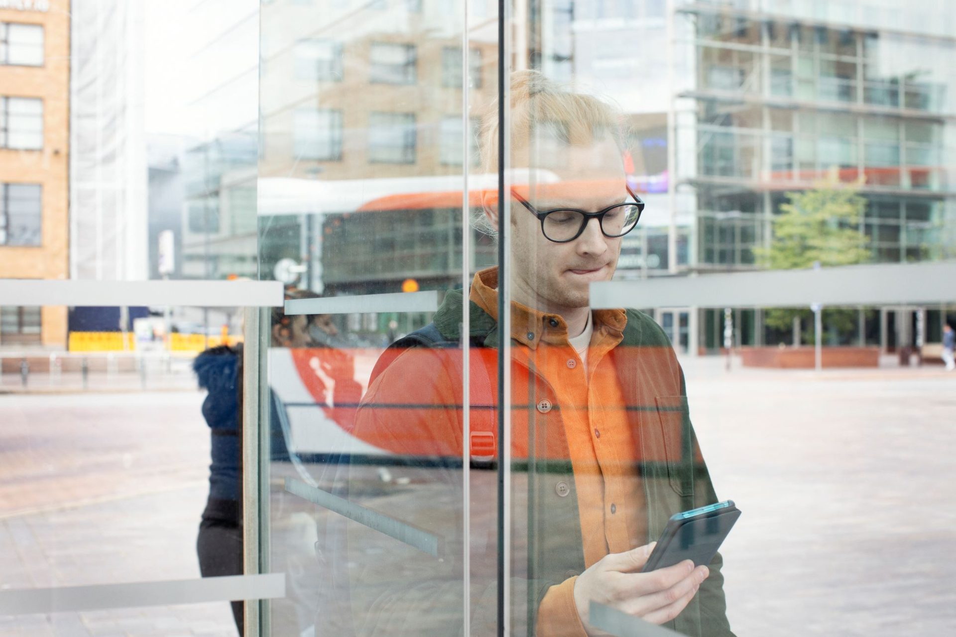 Nuori mies bussipysäkillä katsoo mietteliäänä puhelintaan.