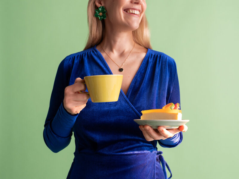 Nainen hymyilee kakkupala ja kahvikuppi käsissään.